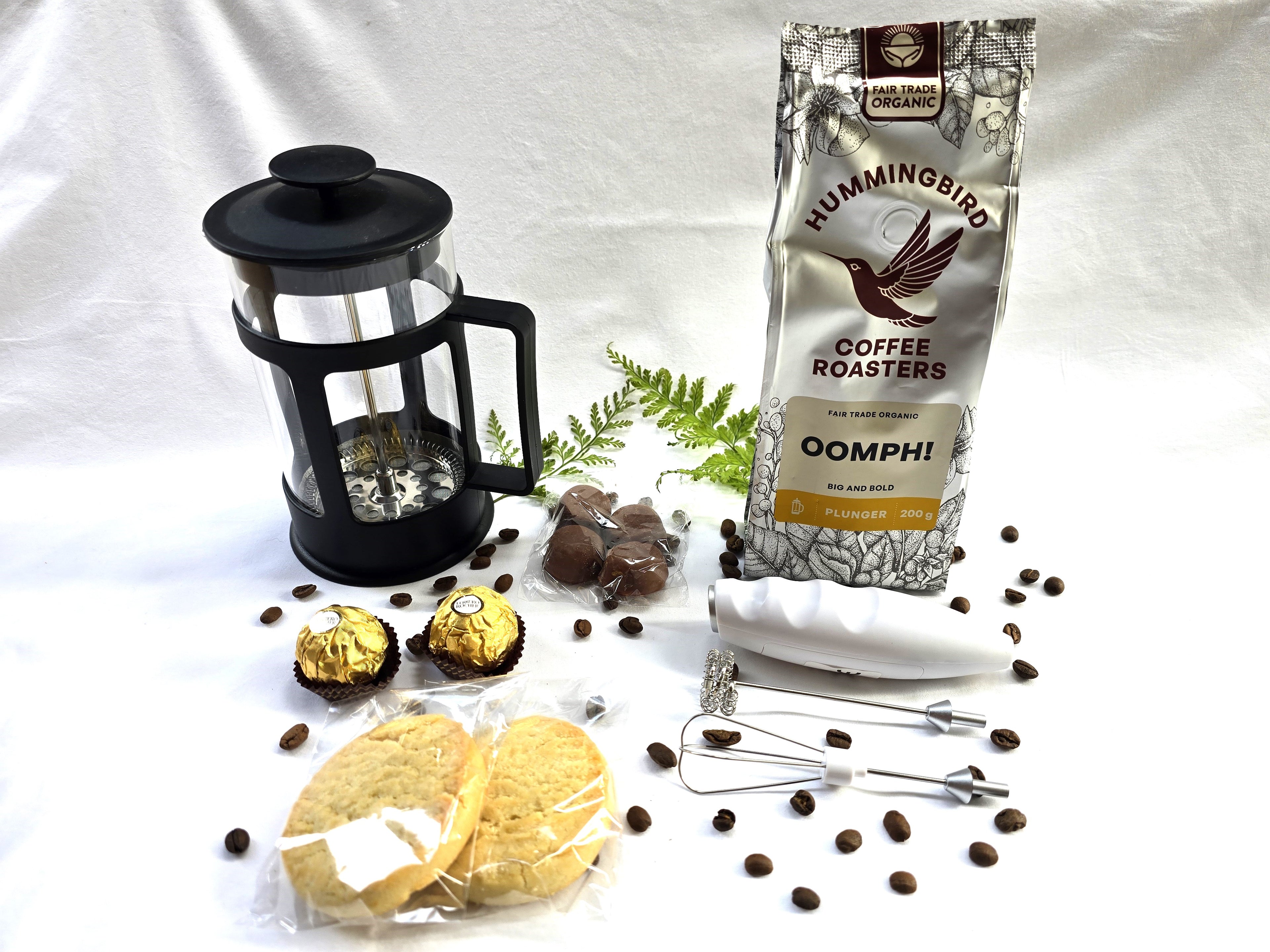 Bag of Hummingbird Coffee Roasters Oomph! coffee, French press, cookies, and chocolate truffles on a white background