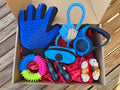 Assorted pet grooming tools including a blue grooming glove, chew toys, and a retractable leash in a cardboard box.